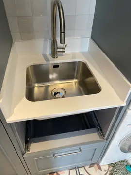Encimera blanca con fregadero de acero. Encimera blanca con copetes laterales y fregadero de acero bajo encimera, en un mueble de lavadero.