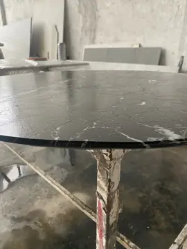 Tapa redonda negra en el taller. Tapa circular negra con vetas blancas y canto recto pulido, apoyada en un caballete del taller.