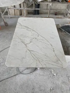 Tapa rectangular blanca con veta ocre. Tapa de esquinas redondeadas en blanco con vetas grises y ocres, apoyada en el taller.