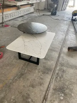 Mesas bajas en negro y blanco en el taller. Tapa redonda negra con veta blanca y tapa rectangular blanca veteada sobre base metálica negra, en la nave del taller.