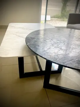 Detalle de las mesas bajas y sus bases. Canto de la tapa redonda negra sobre la tapa blanca veteada y bases metálicas negras, junto a un ventanal.