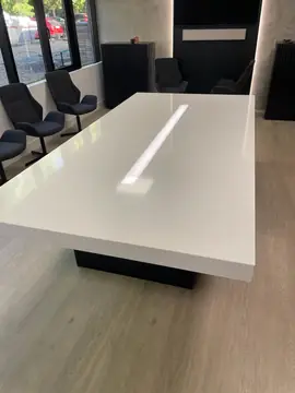 Mesa de reuniones con franja de luz. Tapa blanca brillante de canto grueso con una franja iluminada en el centro, en una sala de reuniones.
