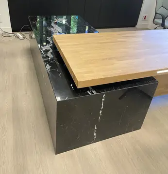Mesa de despacho con pedestal negro veteado. Pedestal negro pulido con vetas blancas sobre el que apoya una tapa en tono madera.