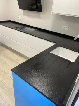 Encimera negra en L con escurridor. Encimera negra texturizada en L con fregadero bajo encimera y escurridor ranurado, sobre muebles aún con film de protección.