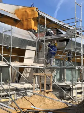 Operario colocando piezas desde el andamio. Colocación de piezas del aplacado desde el andamio sobre la fachada con aislamiento proyectado.
