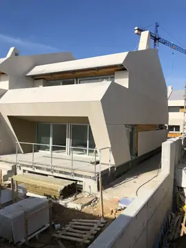 Volumen de fachada aplacado. Fachada de volúmenes quebrados revestida con aplacado en tono crema, con palés y material aún en la terraza inferior.