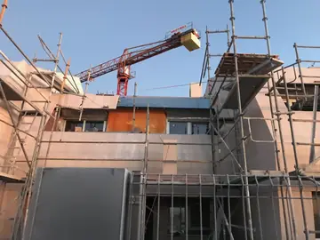 Fachada entre andamios con grúa. Fachada en obra con andamios a ambos lados, parte del aplacado colocado y la grúa al fondo.