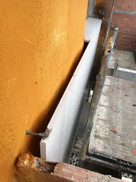 Anclaje de una pieza del aplacado. Detalle del anclaje metálico que sujeta una pieza en tono claro separada del aislamiento proyectado.