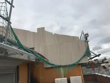 Peto aplacado con red de seguridad. Coronación de la fachada con piezas en tono crema colocadas a distintas alturas y red de seguridad delante.