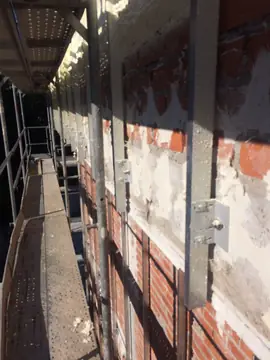 Subestructura desde el andamio. Perfiles y escuadras de anclaje sobre el muro parcheado con mortero, vistos desde la plataforma del andamio.