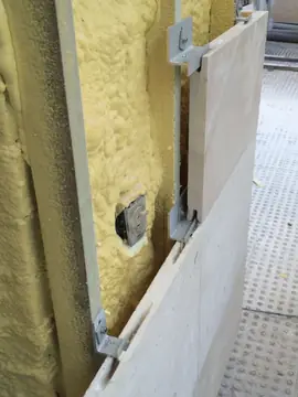 Pieza colgada de su grapa. Pieza en tono crema encajada en las grapas del perfil, con el aislamiento proyectado detrás.