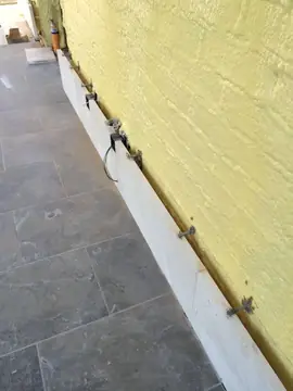 Zócalo en montaje junto al solado oscuro. Hilada inferior del aplacado con sus varillas de anclaje al muro aislado, junto a un solado gris oscuro.