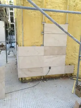 Aplacado a media altura. Varias hiladas de piezas en tono crema sobre el aislamiento, con andamio y una caja de enchufe ya encastrada.