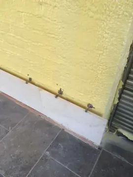 Zócalo con varillas de anclaje. Hilada inferior en tono crema junto a un solado gris oscuro, con las varillas de anclaje al muro todavía a la vista.