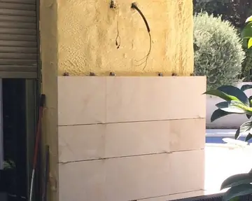 Paño de aplacado sobre el aislamiento. Tres hiladas de piezas en tono crema con veta suave sobre el aislamiento, con los anclajes de la siguiente a la vista.