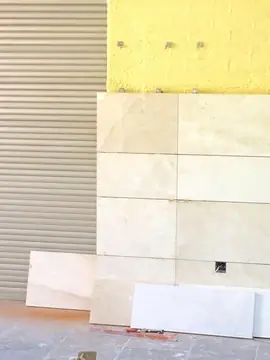 Aplacado junto a persiana metálica. Hiladas de piezas en tono crema con veta suave junto a una persiana, con grapas a la espera sobre el aislamiento.