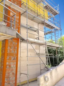 Fachada aplacada con andamio. Paño en tono crema ya colocado bajo el andamio, junto a un machón de ladrillo todavía sin revestir.
