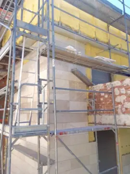 Andamio en fachada en proceso. Fachada con aplacado en tono crema en la parte baja, aislamiento amarillo arriba y un tramo de ladrillo por cubrir.