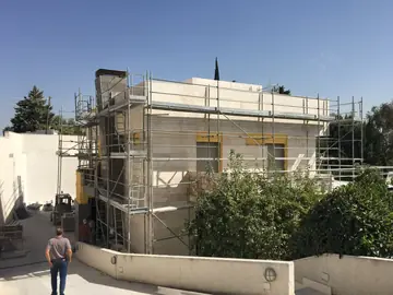 Vivienda con andamio perimetral. Vista general de la vivienda con el aplacado en tono crema avanzado y el andamio perimetral montado.