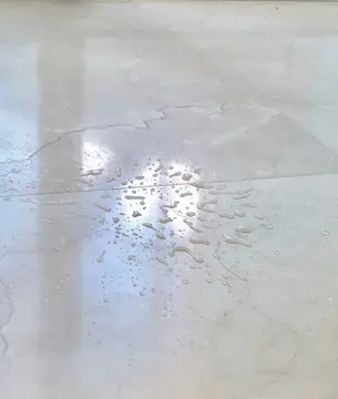 Gotas de agua sobre pavimento pulido. Detalle de gotas de agua sobre el pavimento pulido en tono crema, con la junta entre piezas y el reflejo de la luz.