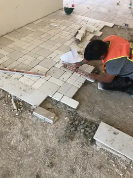 Colocación de pavimento modular en tono crema. Operario marca con nivel y lápiz las piezas en tono crema de cantos redondeados que forman el pavimento modular.