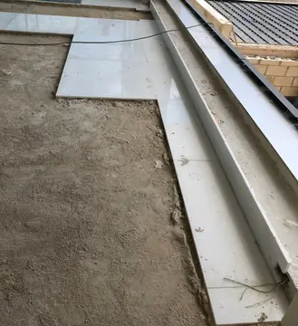 Pavimento y escalón blancos en colocación. Piezas blancas pulidas en el pavimento y en el escalón junto al ventanal, con parte del soporte aún por cubrir.