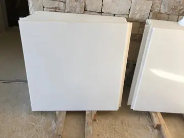 Piezas blancas pulidas en acopio. Dos pilas de piezas blancas pulidas apoyadas sobre listones de madera delante de un muro de mampostería.