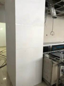 Pilar revestido en piezas blancas. Pilar aplacado con piezas blancas de gran formato junto a muebles de acero inoxidable, con el techo y las instalaciones aún por terminar.