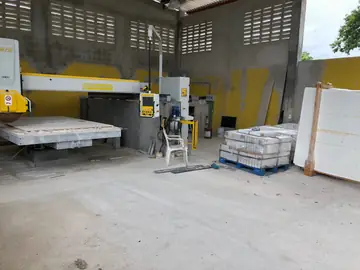 Taller con cortadora de puente. Nave de taller con cortadora de puente, palés de piezas blancas cortadas y un tablero en caballete.