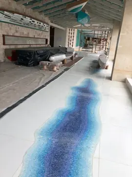 Pasillo con río de mosaico en el pavimento. Pavimento blanco en piezas grandes con un río de mosaico azul, mientras el mobiliario sigue protegido.