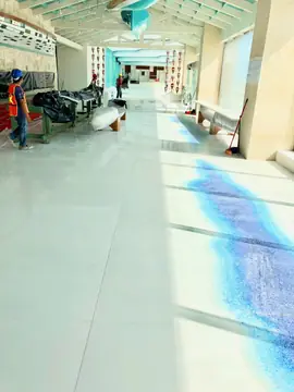 Galería con pavimento blanco y mosaico azul. Galería abierta con pavimento blanco pulido y mosaico azul, con operarios terminando al fondo.