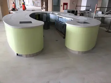Isla de buffet en forma de herradura. Isla curva con encimera blanca, placas encastradas y frente verde, con los equipos aún por terminar.