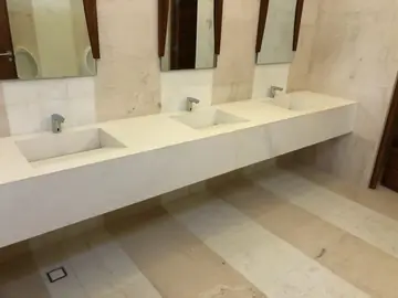 Lavabo corrido con tres senos integrados. Encimera blanca volada con tres senos integrados, paredes aplacadas en tono crema y suelo a franjas.