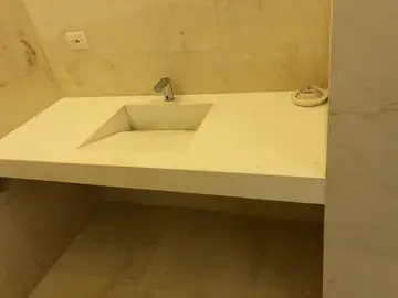 Lavabo volado con seno integrado. Detalle de la encimera clara con seno integrado y grifo, entre paredes aplacadas en tono crema.