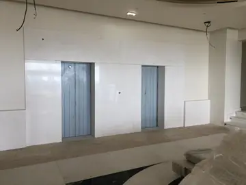 Revestimiento blanco en vestíbulo de ascensores. Pared de ascensores revestida con piezas blancas de gran formato, con la instalación eléctrica aún por rematar.
