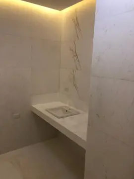 Aseo aplacado con encimera y lavabo. Paredes aplacadas en blanco con vetas marrones y encimera volada del mismo tono con lavabo.