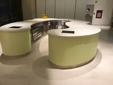 Isla de buffet terminada. Isla curva con encimera blanca, placas encastradas y frente verde, ya terminada sobre pavimento claro.