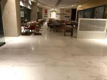 Restaurante con pavimento claro con vetas. Vista general del restaurante con pavimento claro con vetas, columnas revestidas en tono crema y mesas montadas.