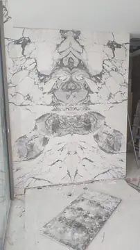 Paño de vetas casadas en espejo. Revestimiento de pared en piezas blancas con veta gris casadas en espejo, con una pieza suelta apoyada en el suelo durante la colocación.