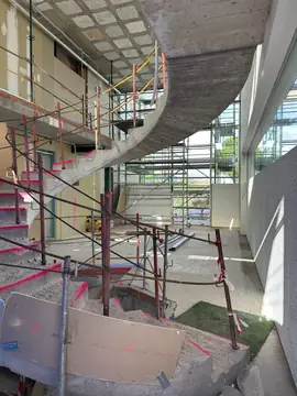 Escalera curva en fase de estructura. Escalera curva de hormigón aún sin revestir, rodeada de andamios y barandillas provisionales.