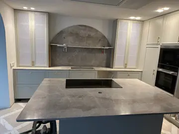 Cocina con isla y frente en arco. Isla con encimera gris de veta clara y frente de cocina en arco revestido en el mismo tono.
