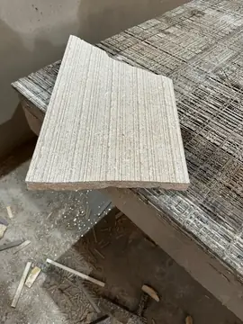 Pieza de piedra con cara estriada. Pieza de piedra beige con la cara labrada en estrías, apoyada sobre otras piezas con malla en el reverso.