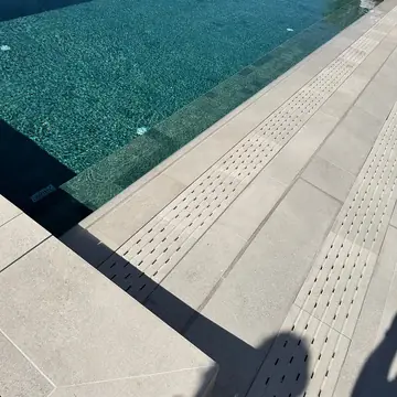 Piscina con playa en piezas claras. Piscina llena junto a una playa en piezas claras con bandas ranuradas a lo largo del borde.