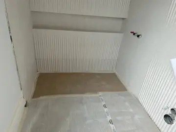 Baño con revestimiento acanalado. Baño en obra con paredes en revestimiento blanco de relieve acanalado y el suelo aún protegido.