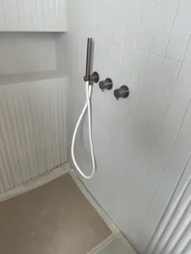 Ducha con grifería en tono bronce. Ducha con revestimiento claro en piezas verticales y paños acanalados, grifería en tono bronce y suelo aún protegido.