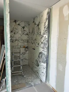 Ducha revestida en blanco veteado. Cabina de ducha revestida en piezas blancas de veta oscura, con escalera y placas aún sin rematar alrededor.