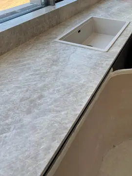 Montaje de encimera con fregadero. Encimera gris clara veteada con fregadero blanco y alféizar a juego, con los muebles aún protegidos con cartón.