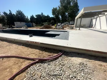 Terraza de piscina en piezas claras. Playa de piscina pavimentada en piezas claras junto al vaso oscuro, con tubos y grava aún en el terreno.