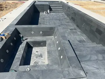 Piscina con spa revestida en gris oscuro. Vaso de piscina revestido en piezas gris oscuro con spa integrado, boquillas y escalera al fondo, antes del llenado.