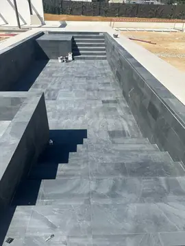 Escalera de acceso a la piscina. Vaso de piscina revestido en piezas gris oscuro con escalera de obra y peldaños del mismo acabado.